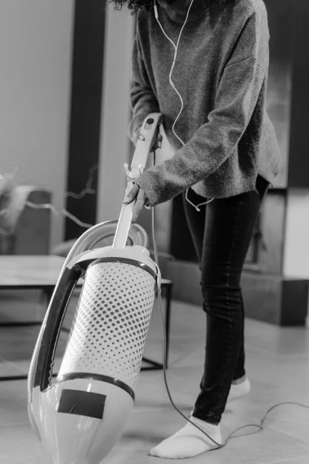Close-up of people cleaning an indoor wooden floor with a broom and dustpan.