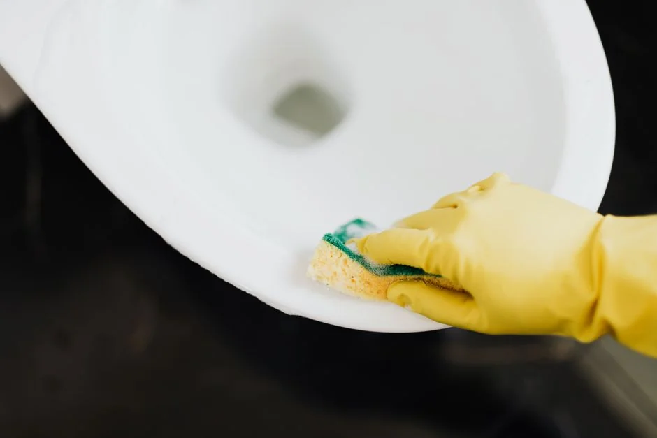 Vue de profil d’une jeune femme concentrée, portant des gants en latex, debout et nettoyant un miroir dans une pièce lumineuse en journée